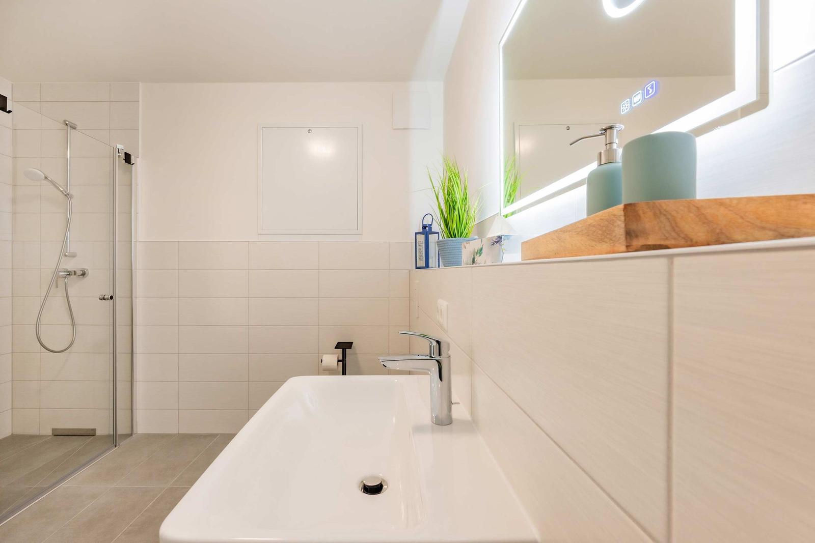 Badezimmer mit Dusche, Waschbecken und beleuchtetem Spiegel.