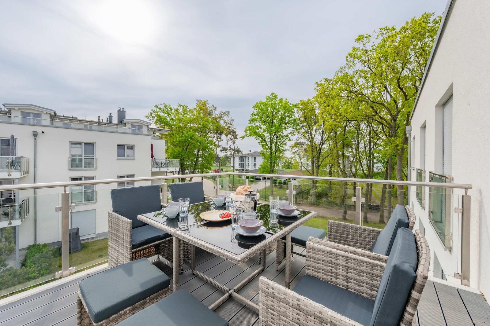 Terrasse mit Sitzgruppe, Tisch und Blick auf Bäume und Gebäude.