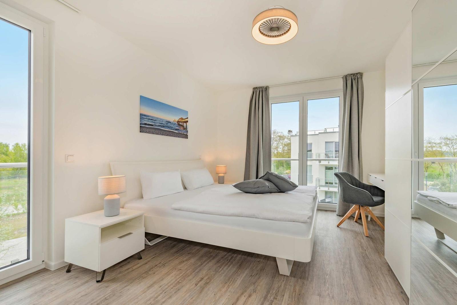 Schlafzimmer mit Bett, Nachttisch, Stuhl und Fenstern.