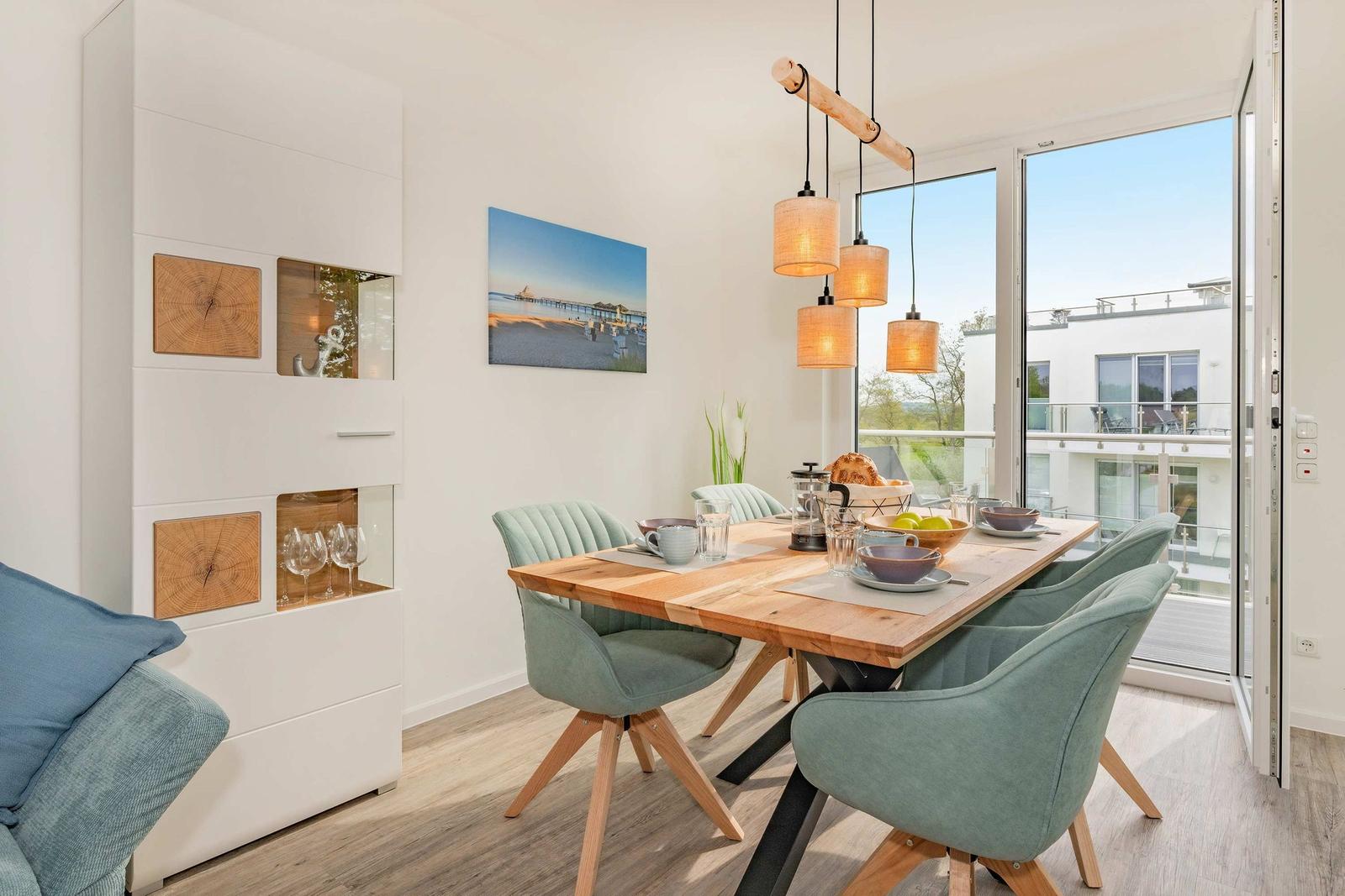 Essbereich mit Holztisch, grünen Stühlen und Glasfront zur Terrasse.