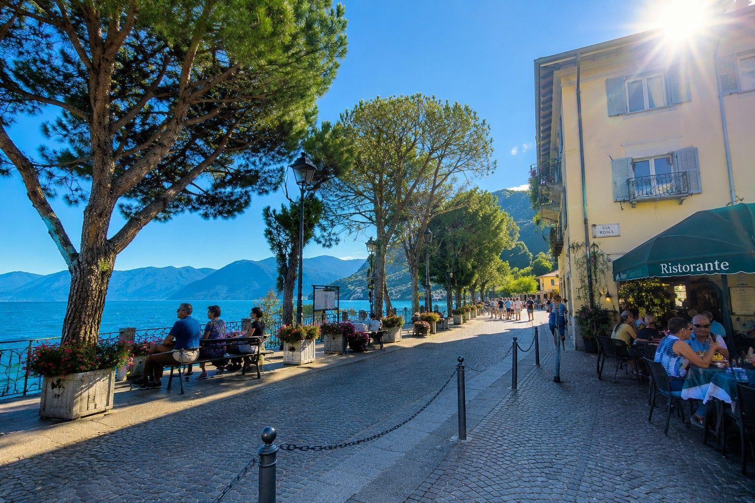 Promenade entlang des Sees mit Bäumen, Restaurants und Blick auf die Berge.