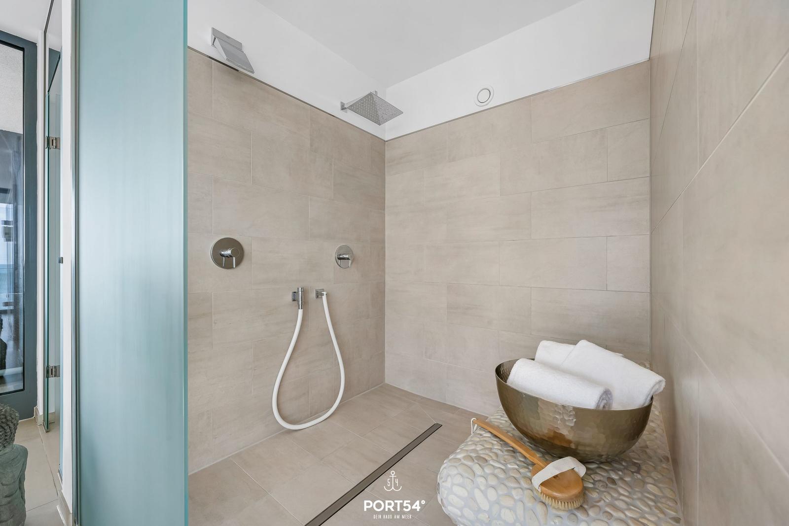 Dusche mit Regenduschkopf und Handbrause, daneben Metallwanne mit Handtüchern.