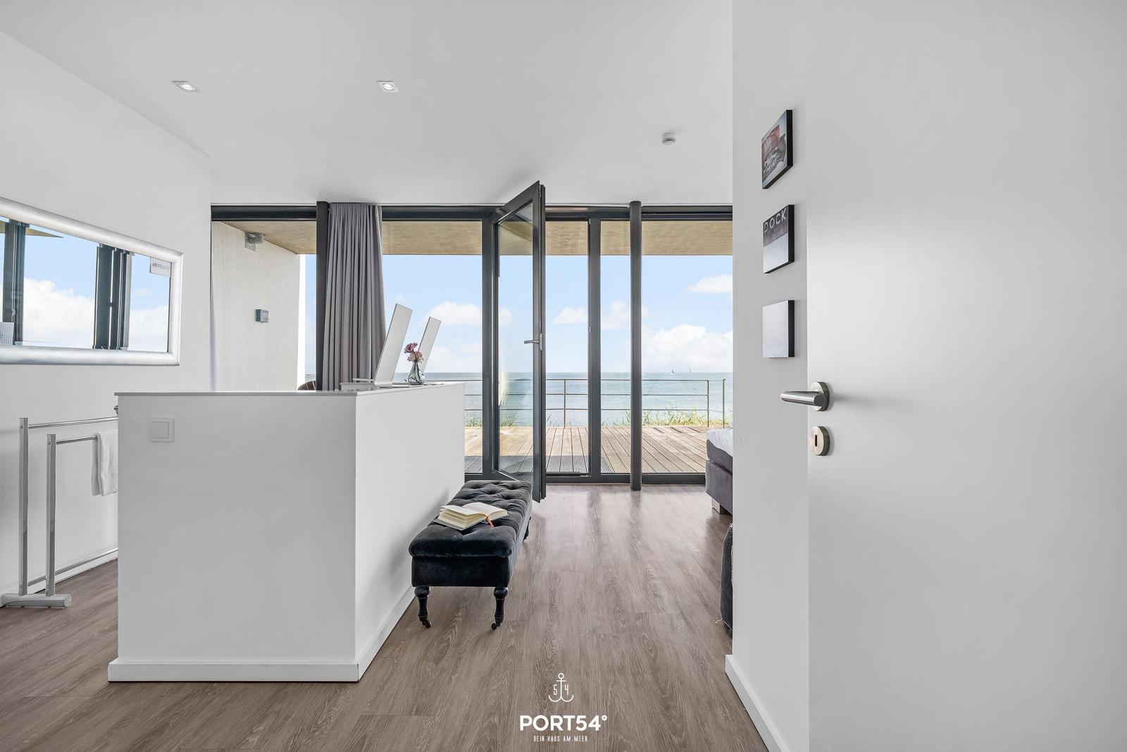 Moderne Wohnung mit Meerblick und Terrasse. Weiße Wände, Holzboden und Glasfront.