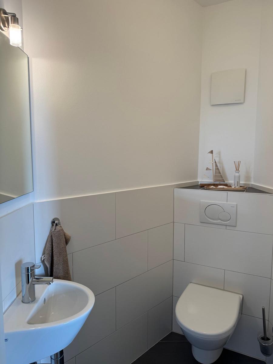 Badezimmer mit Toilette, Waschbecken und Spiegel. Wandverkleidung aus hellen Fliesen.