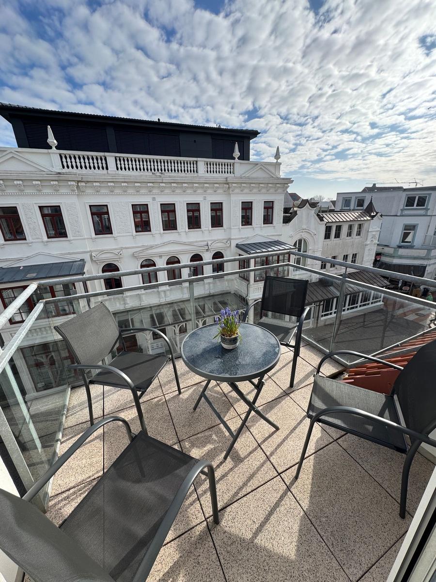 Terrasse mit Tisch und Stühlen. Blick auf historische Gebäude unter blauem Himmel.