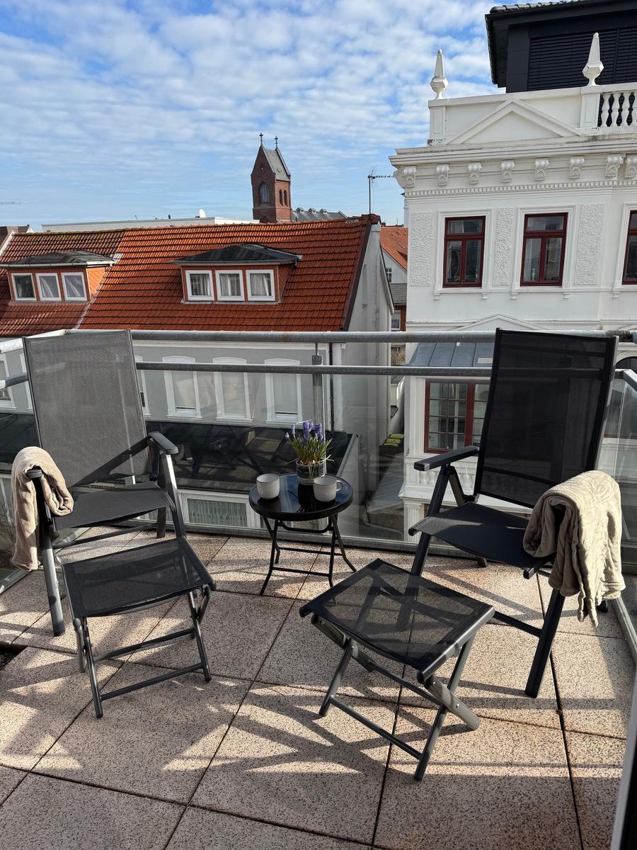 Terrasse mit zwei Stühlen, Tisch und Blick auf Dächer und Turm.