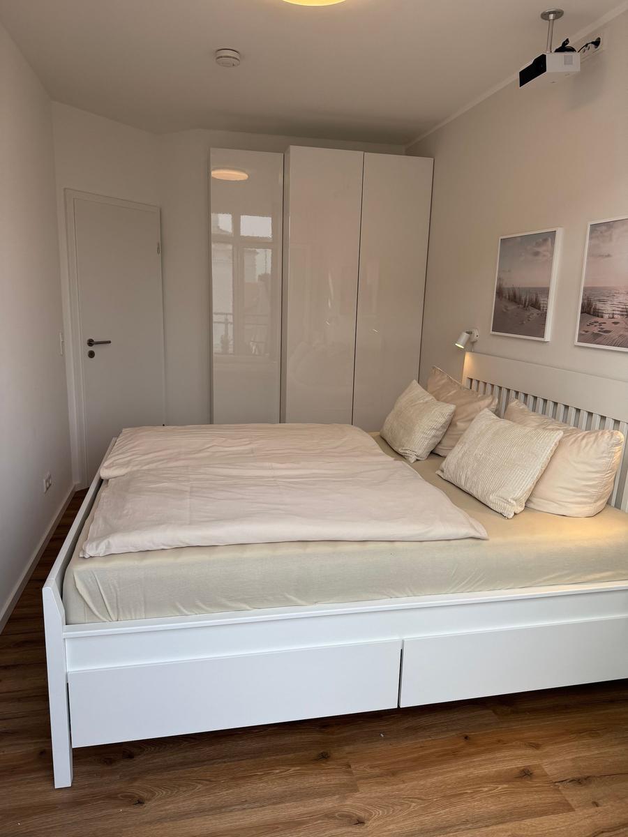 Schlafzimmer mit weißem Bett, Kleiderschrank und Holzboden