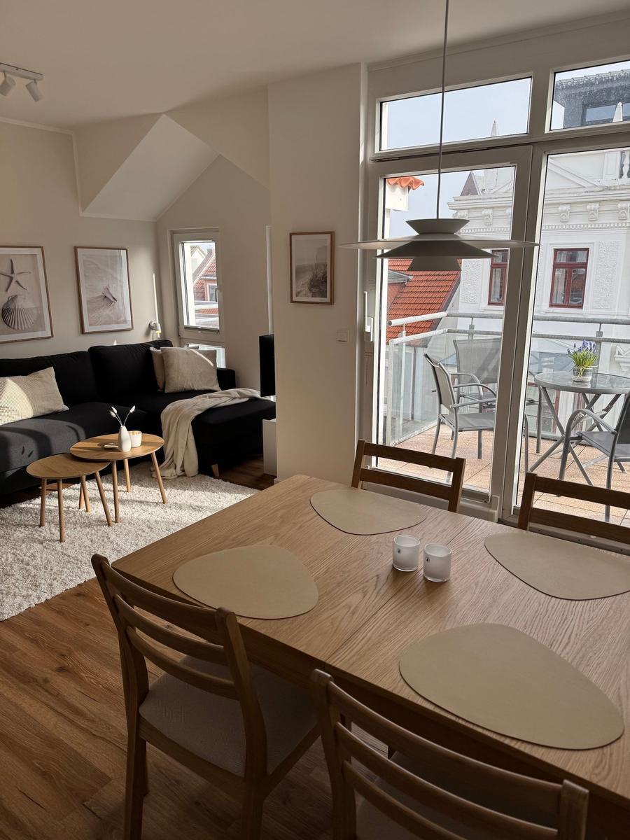 Essbereich mit Holztisch und Stühlen. Wohnbereich mit Sofa und Balkon.