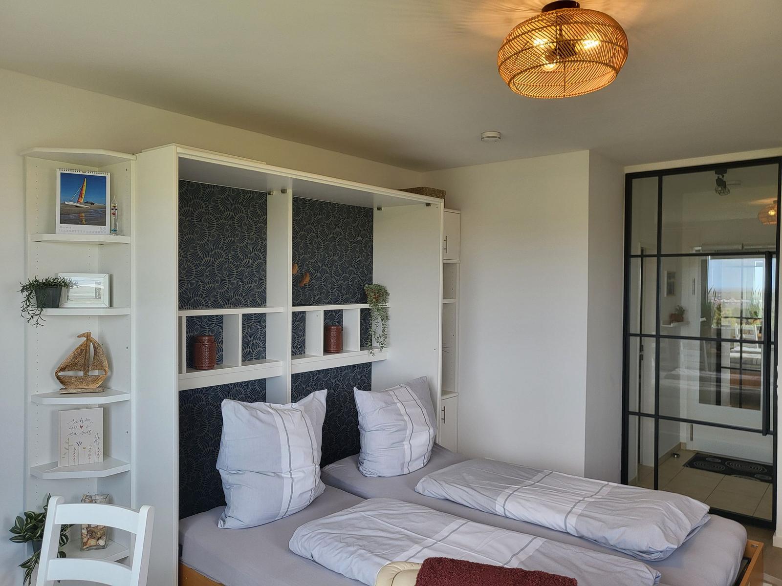 Two beds with white pillows and bedding. Behind the beds is a shelf with decor.