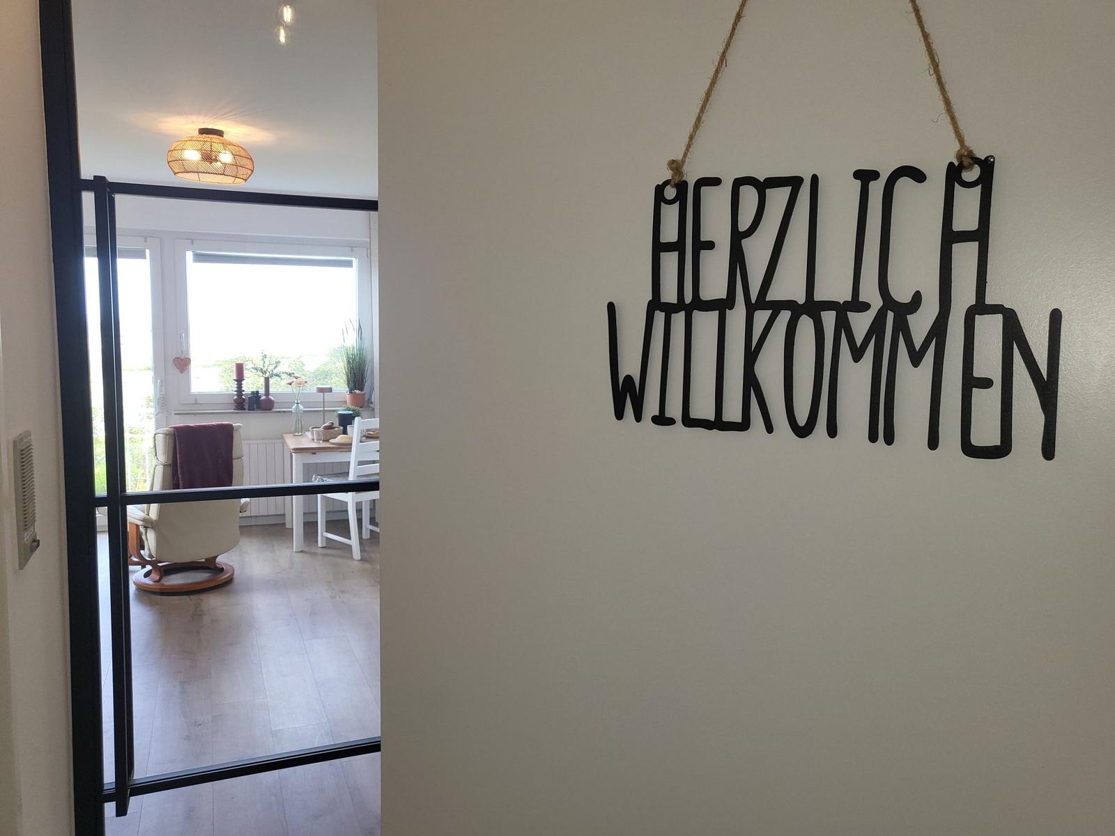 Welcome sign hangs on the wall. Through door, dining room with table and chairs is visible.