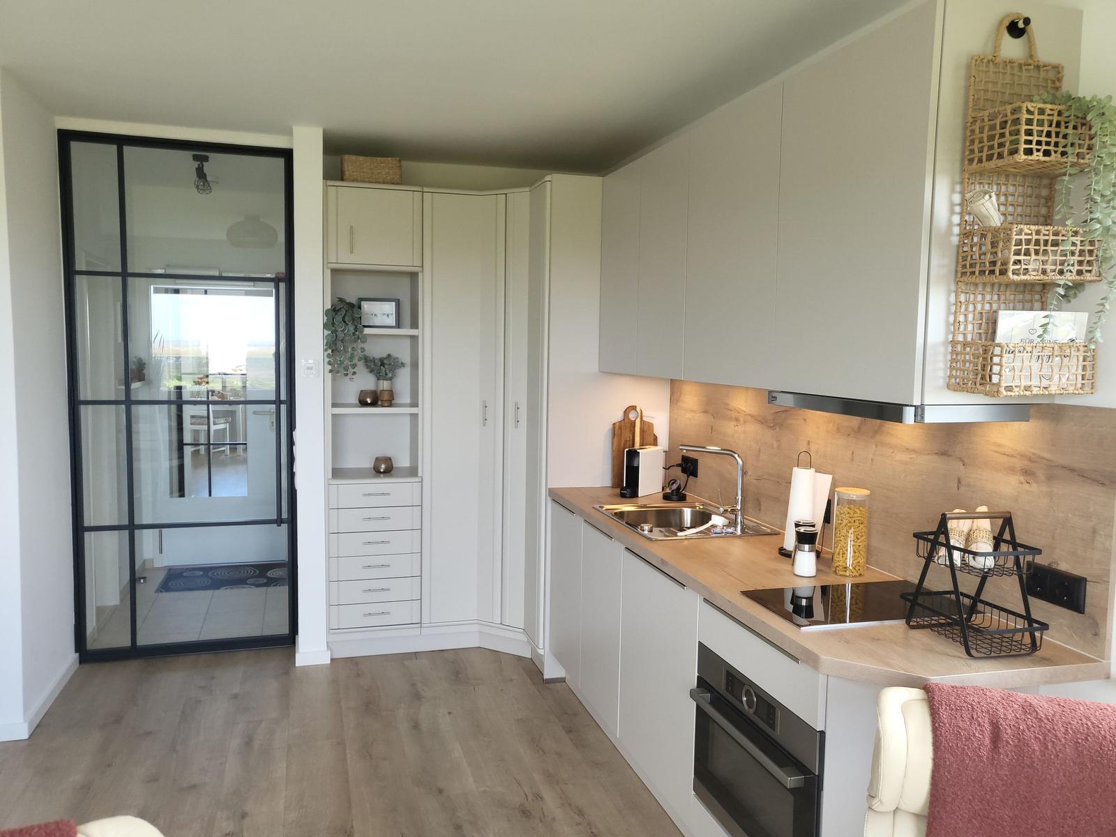 Kitchen with light cabinets, wooden countertop, and built-in oven. Glass wall leads to living area.