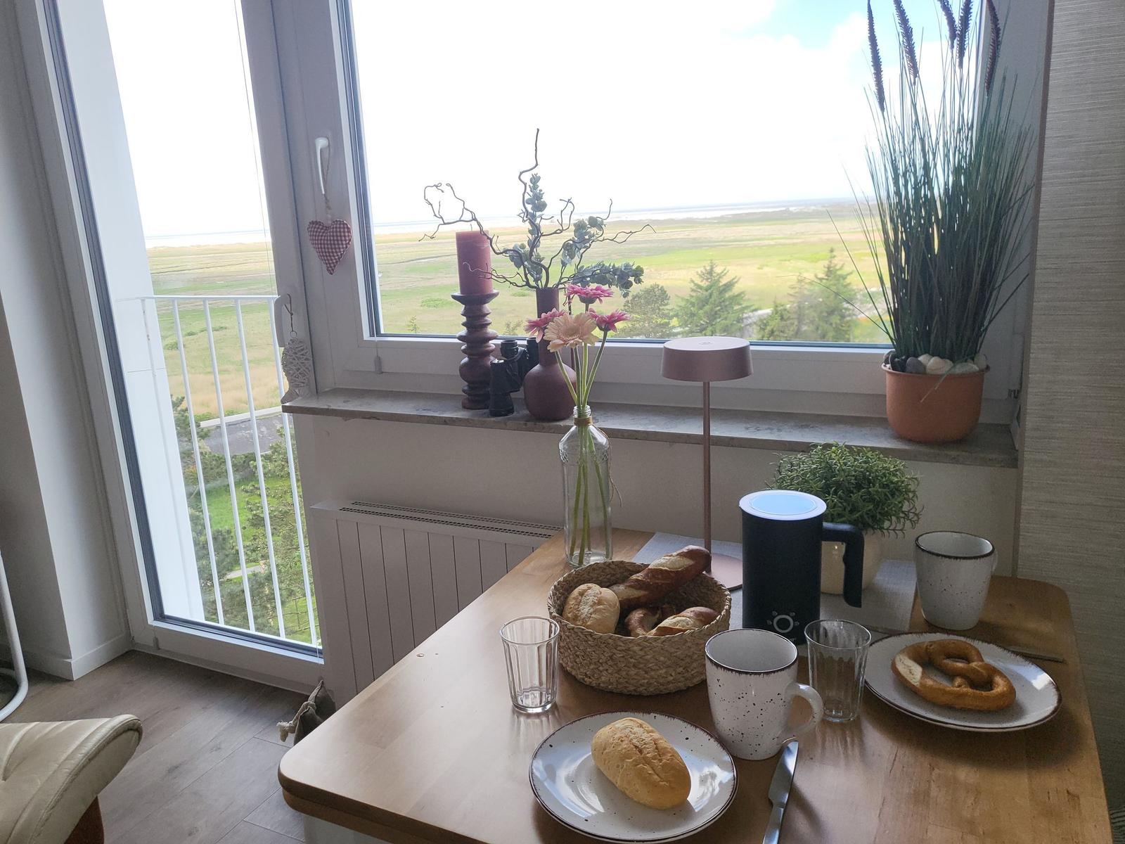 Breakfast table with bread and coffee by large window with view of landscape.