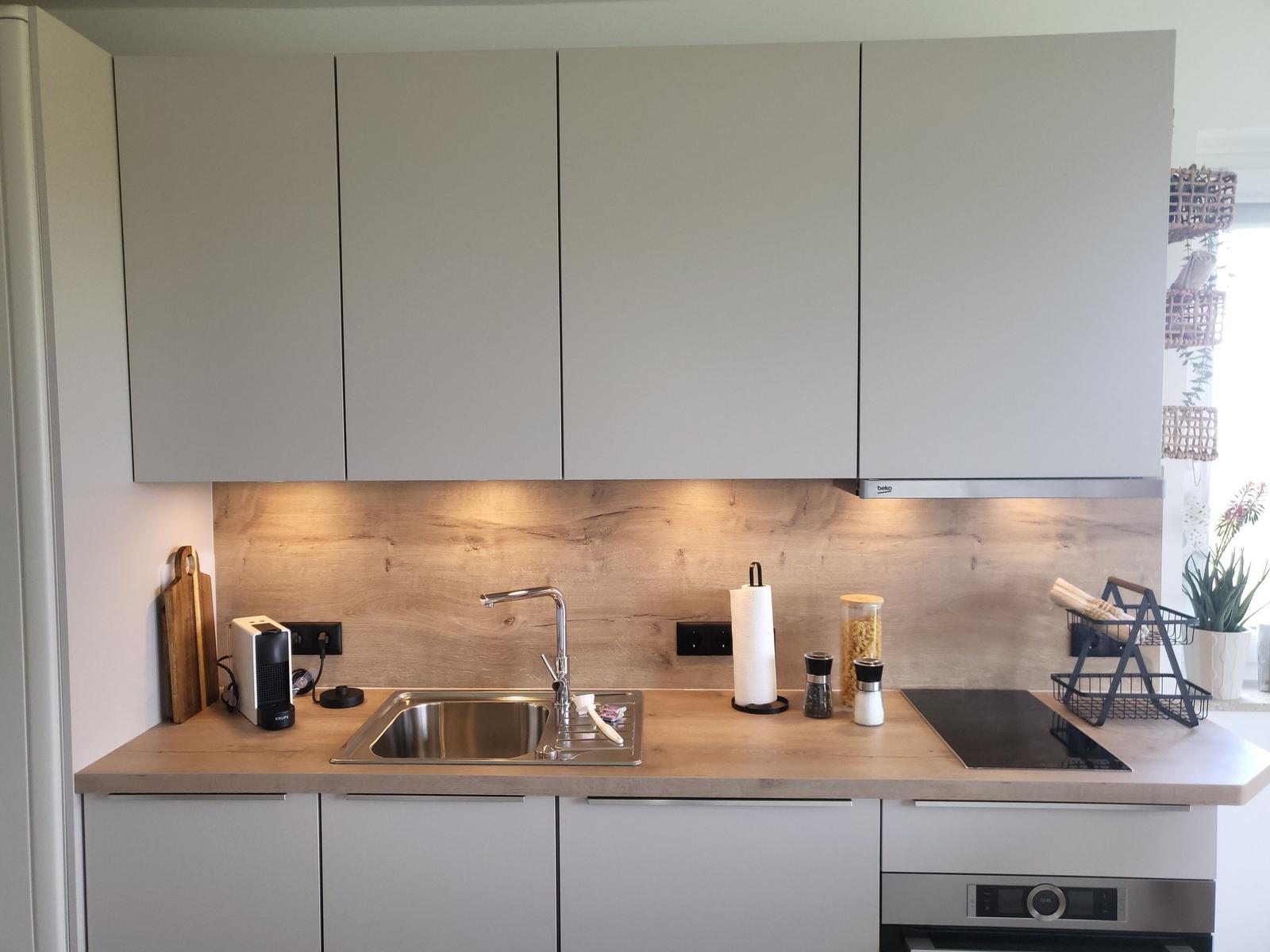 Kitchen with light cabinets, wooden backsplash, and stainless steel sink.
