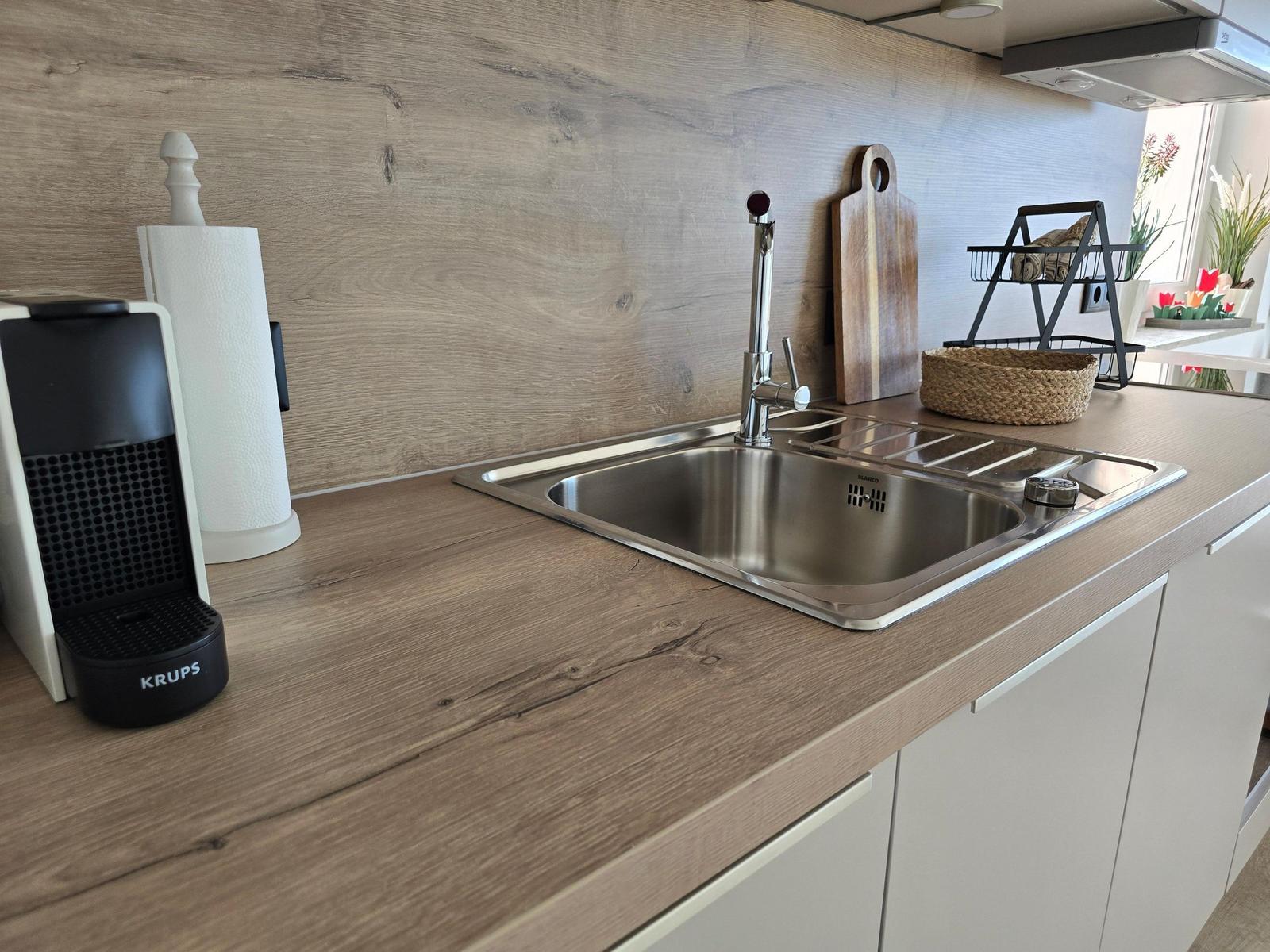 Kitchen counter with stainless steel sink, wooden surface, and kitchen utensils.