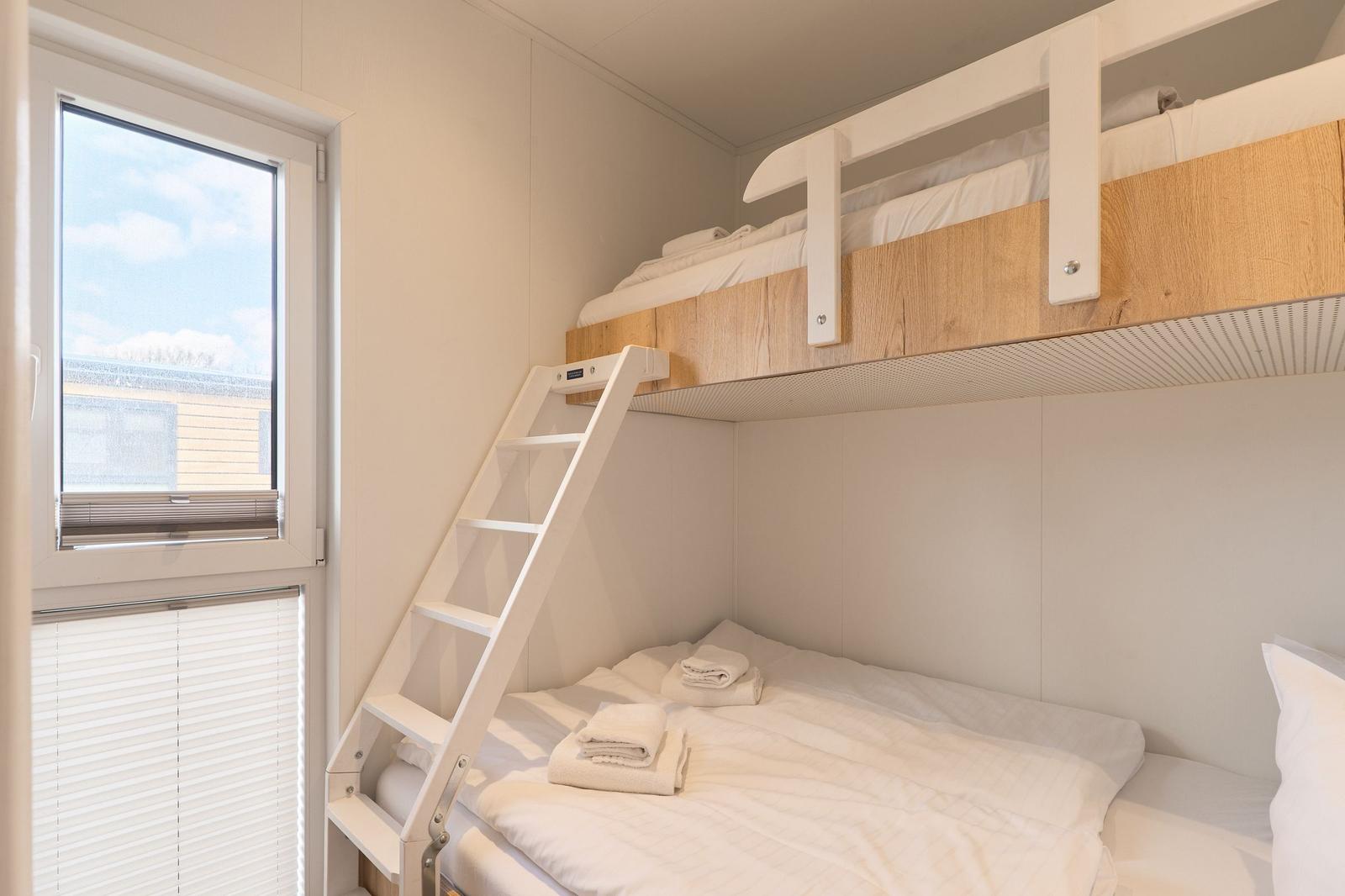 Zimmer mit Hochbett und Treppe, Fenster mit Jalousie, Bett mit weißen Laken und Handtüchern.