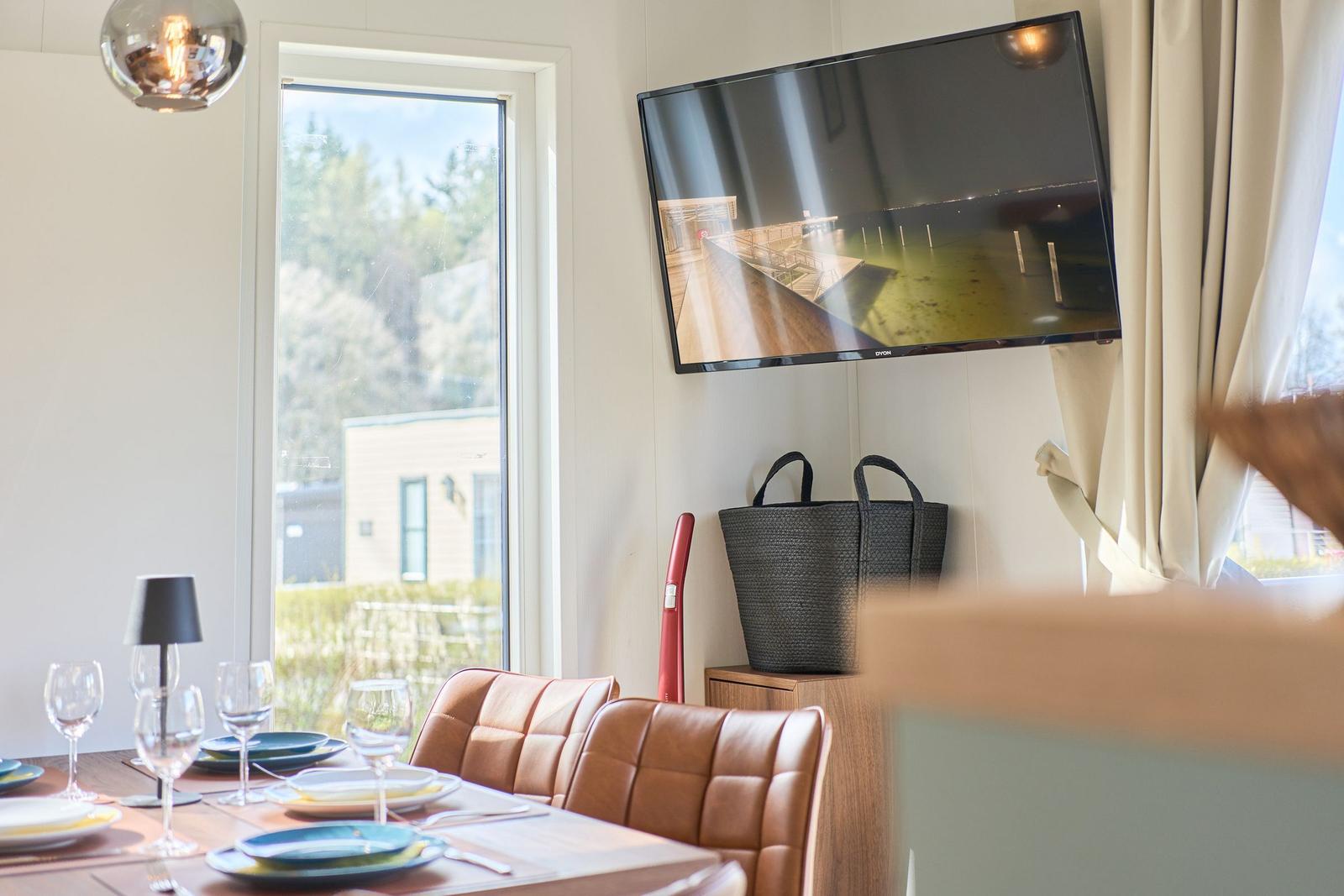 Esszimmer mit Tisch, Stühlen und TV an der Wand. Fenster zeigt Außenbereich.