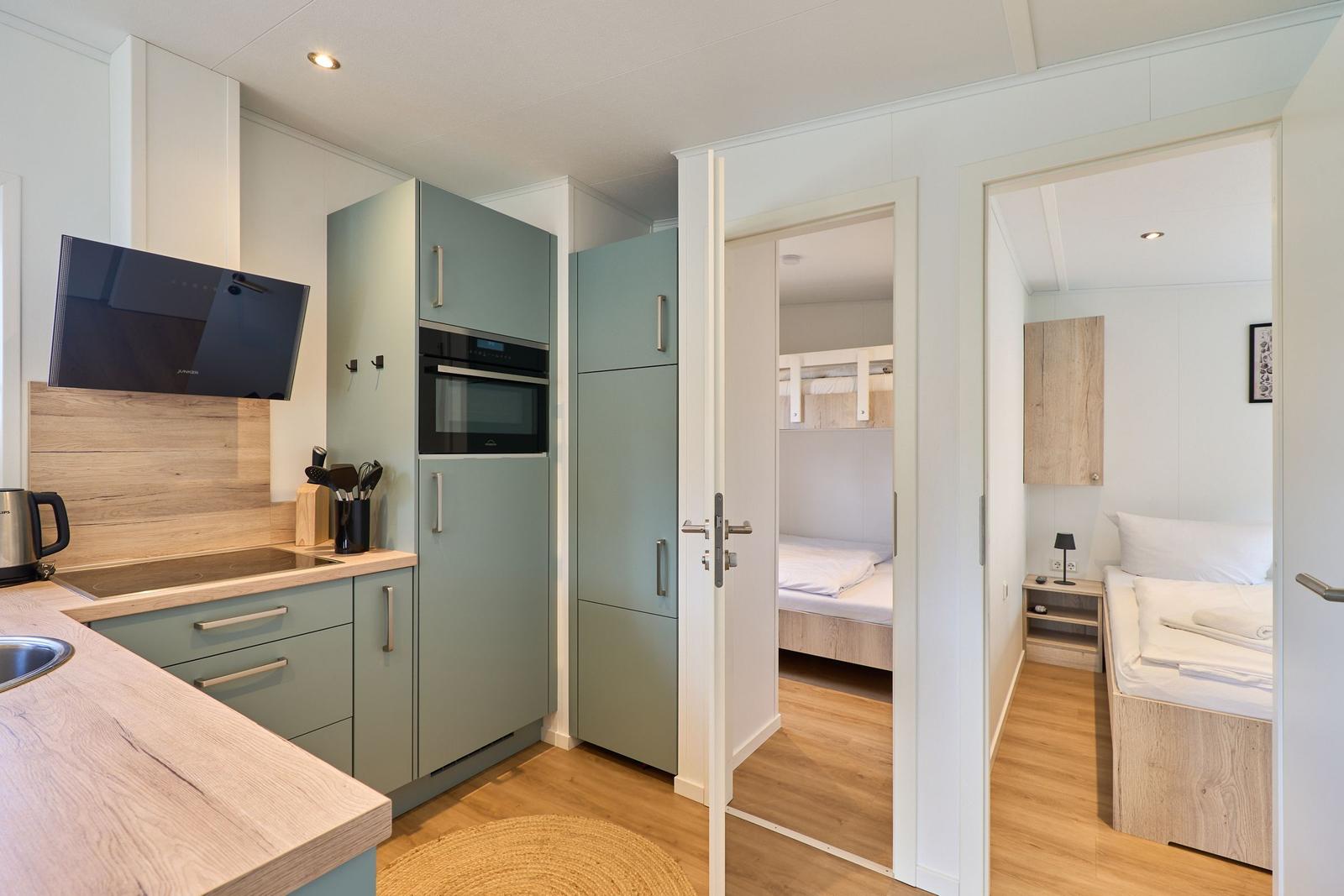 Küche mit hellen Schränken und Blick in zwei Schlafzimmer mit Betten.