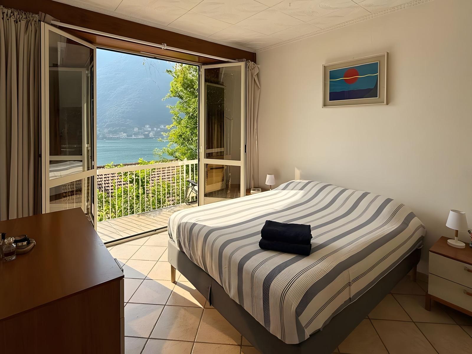 Schlafzimmer mit Blick auf See und Berg. Bett, Nachttische und Balkon.