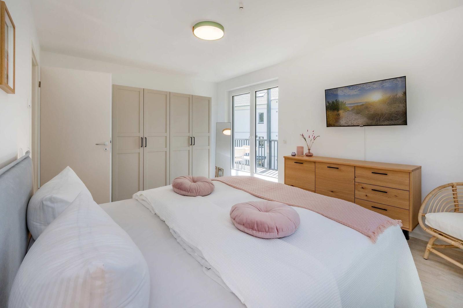 Schlafzimmer mit Bett, Kleiderschrank und TV. Balkon mit Blick auf Außenbereich.