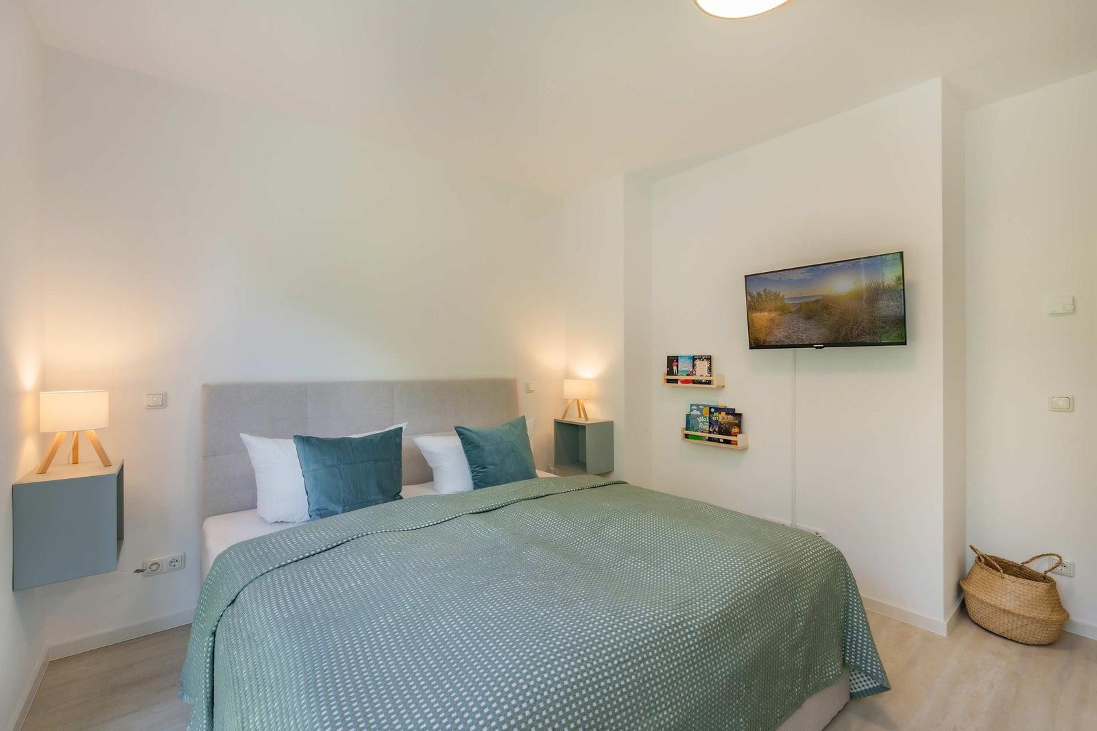 Schlafzimmer mit Bett, Nachttisch und Fernseher an der Wand.