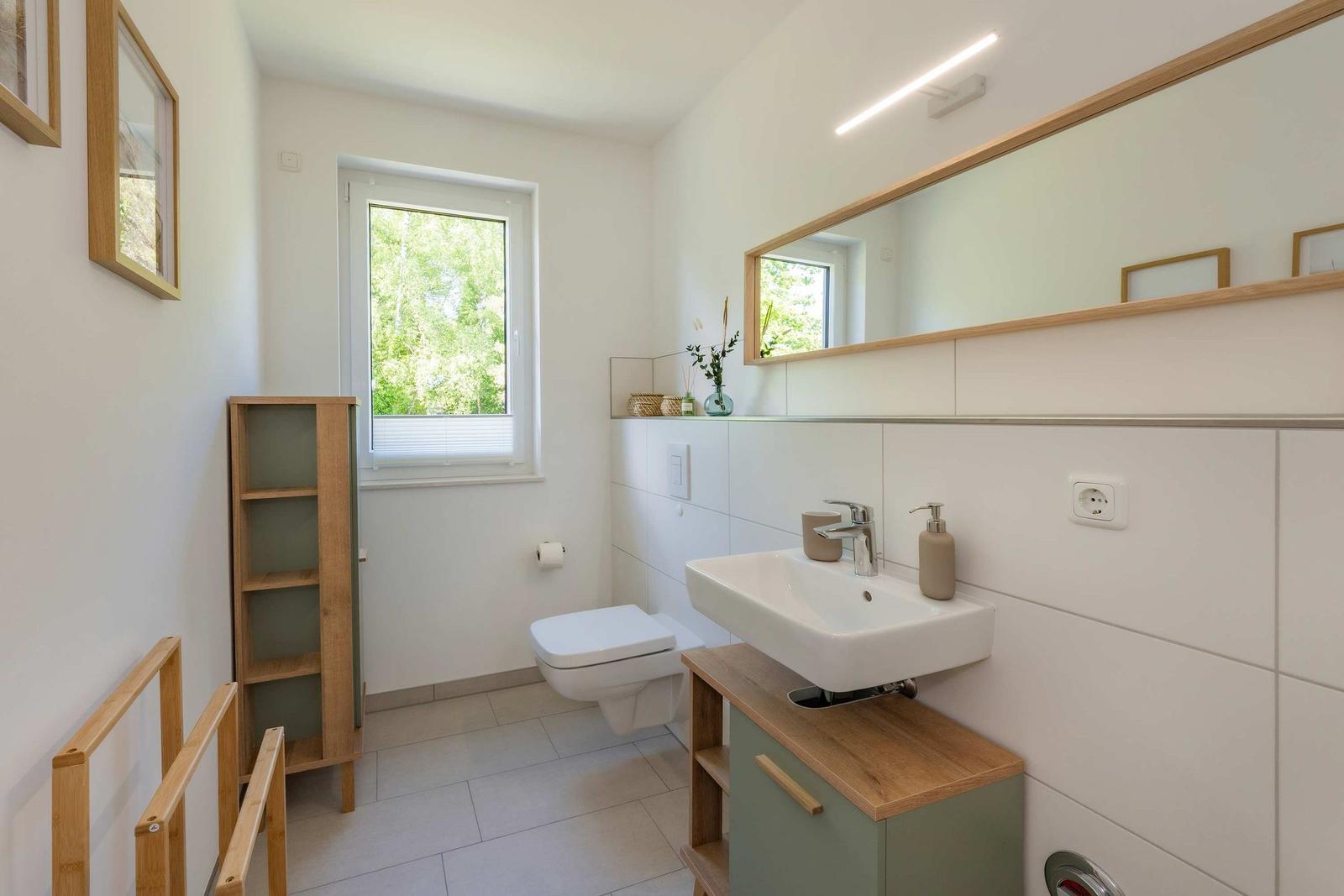 Badezimmer mit Waschbecken, Spiegel, Toilette und Fenster.