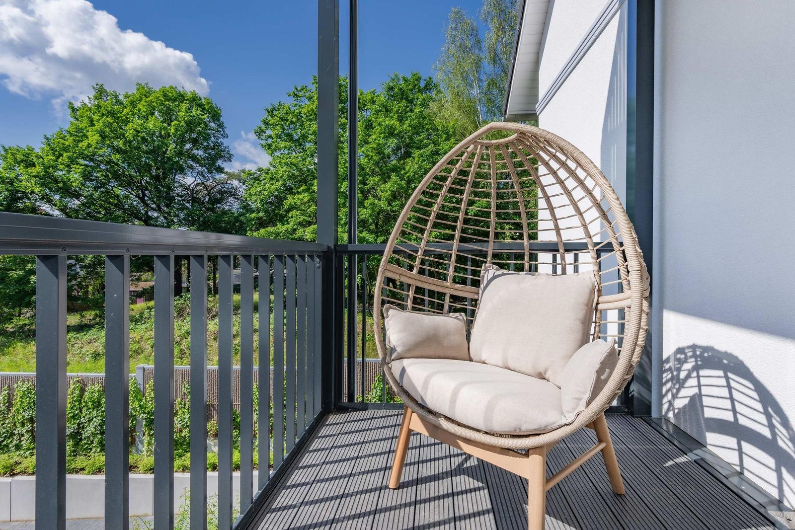 Terrasse mit Hängesessel, Holzboden und Blick auf grüne Bäume.
