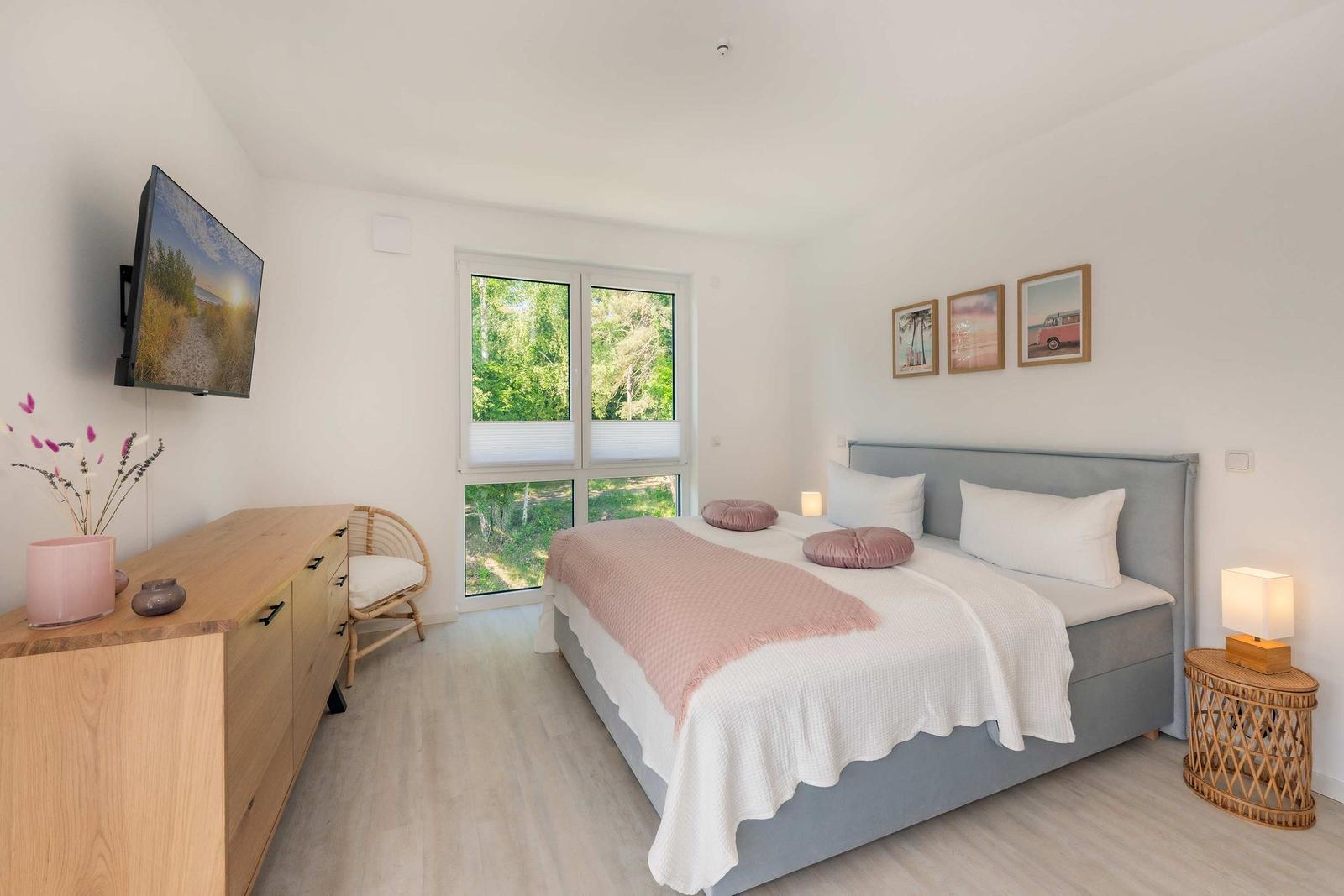 Schlafzimmer mit Bett, Fenster, TV und Nachttisch.