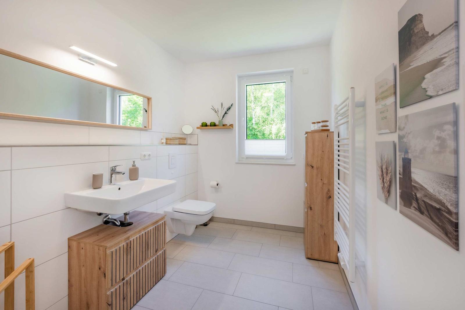 Badezimmer mit Waschbecken, Toilette und Fenster. Holzmöbel und Wandbilder.