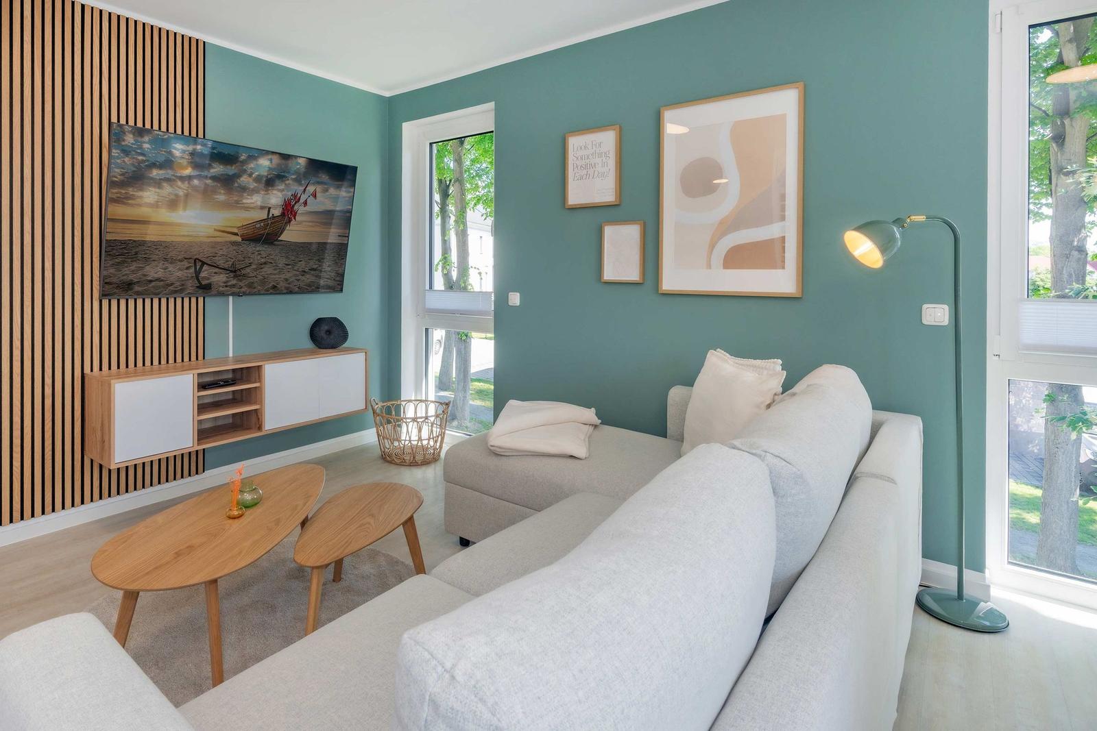 Wohnzimmer mit Sofa, Fernseher und Fenstern