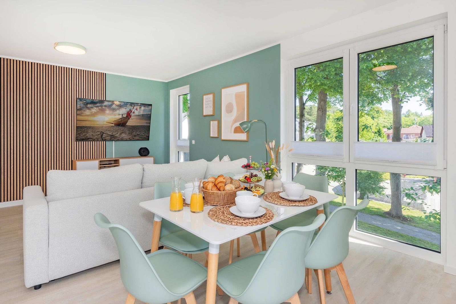 Esszimmer mit Tisch, Stühlen und Blick auf Grün. Wohnbereich mit Sofa und Fernseher.