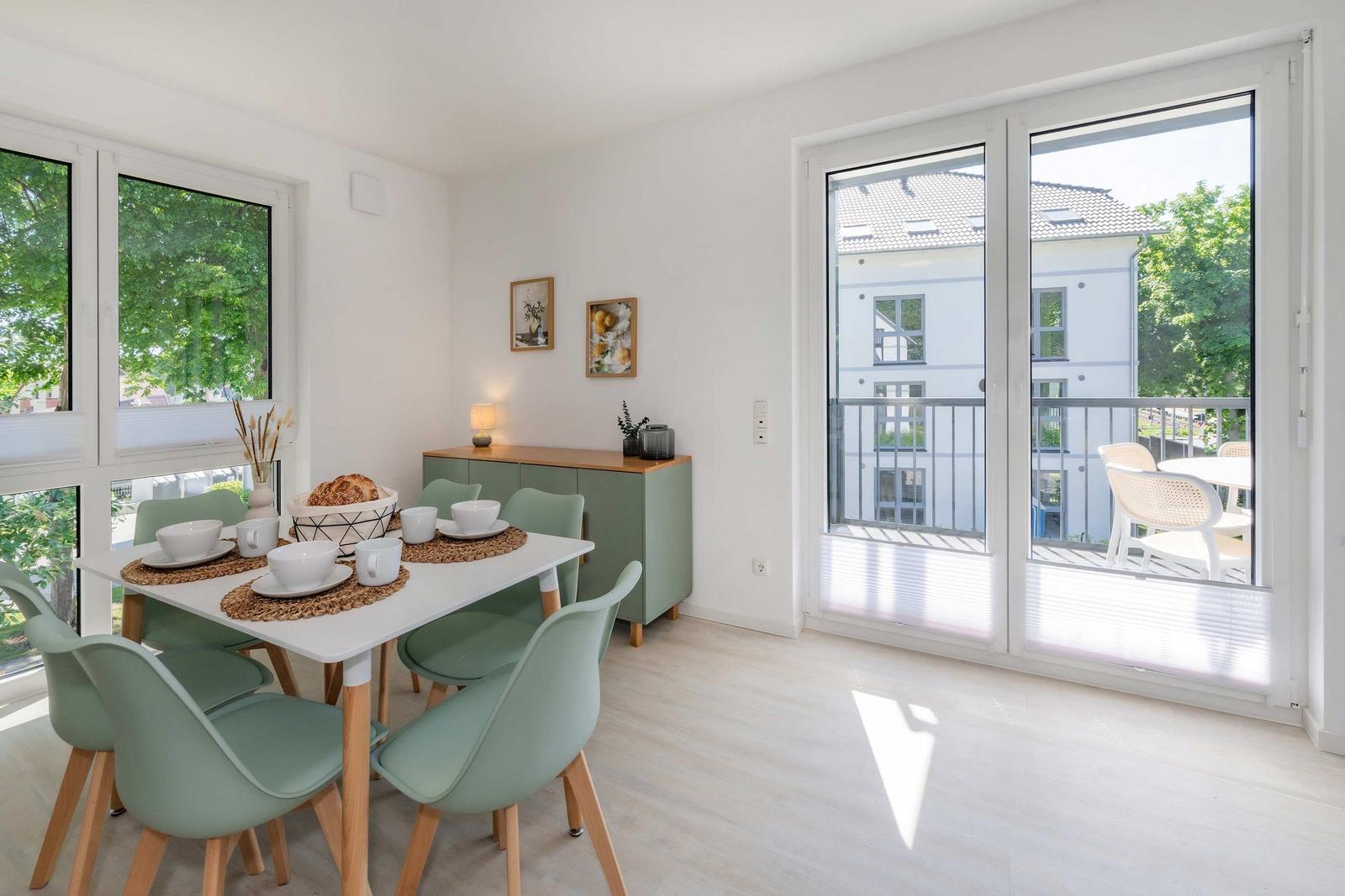 Esszimmer mit Tisch, Stühlen und Blick auf Balkon.