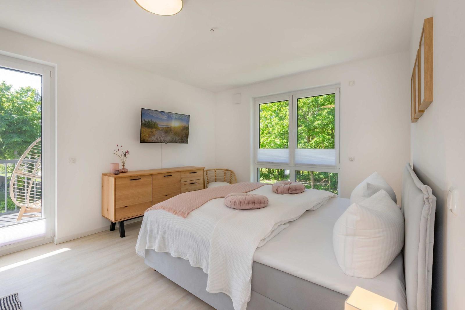 Schlafzimmer mit Bett, TV und Fenstern zum Garten