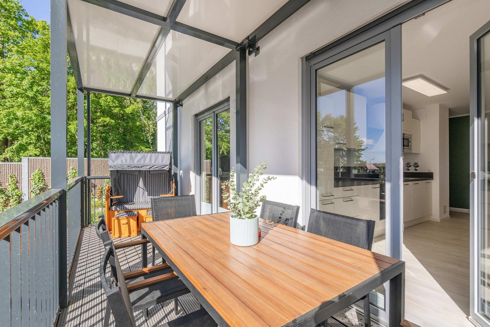 Terrasse mit Holztisch, Stühlen und Pflanze. Durchgehende Glasschiebetüren führen ins Haus.