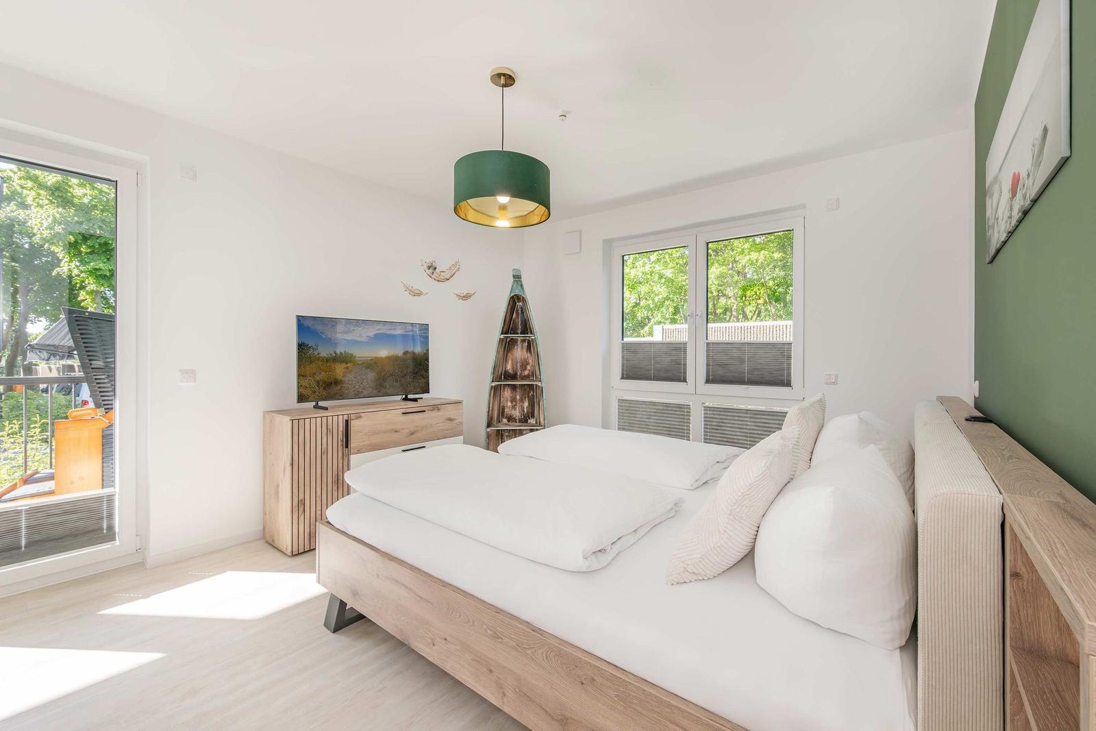 Schlafzimmer mit Bett, Fernseher und Fenstern zum Balkon.