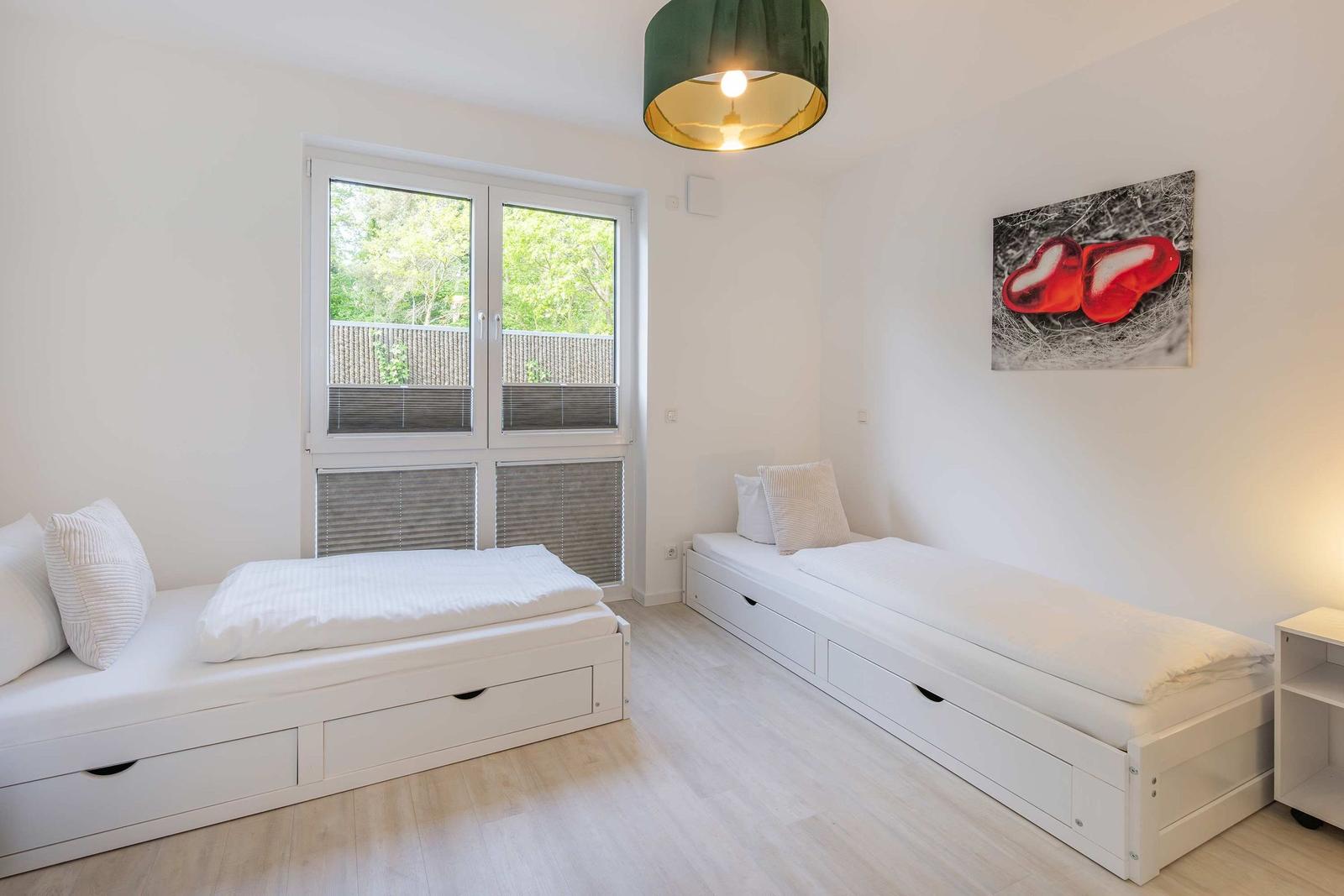 Zwei weiße Schlafsofas mit Stauraum, Fenster mit Blick auf Balkon, Wandbild mit roten Herzen.