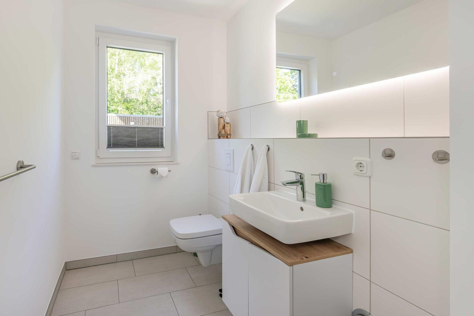 Badezimmer mit Waschbecken, Toilette und Fenster mit Blick auf Grün.
