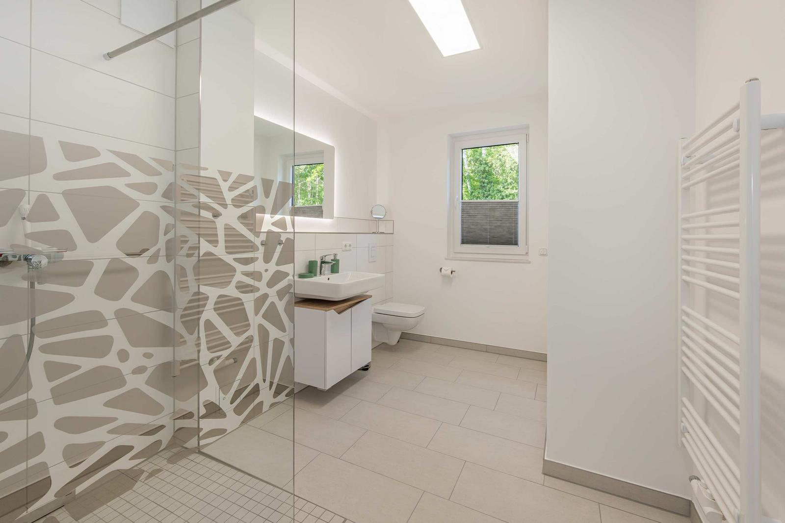 Badezimmer mit Dusche, Waschbecken und Toilette. Fenster mit Blick auf Grün.