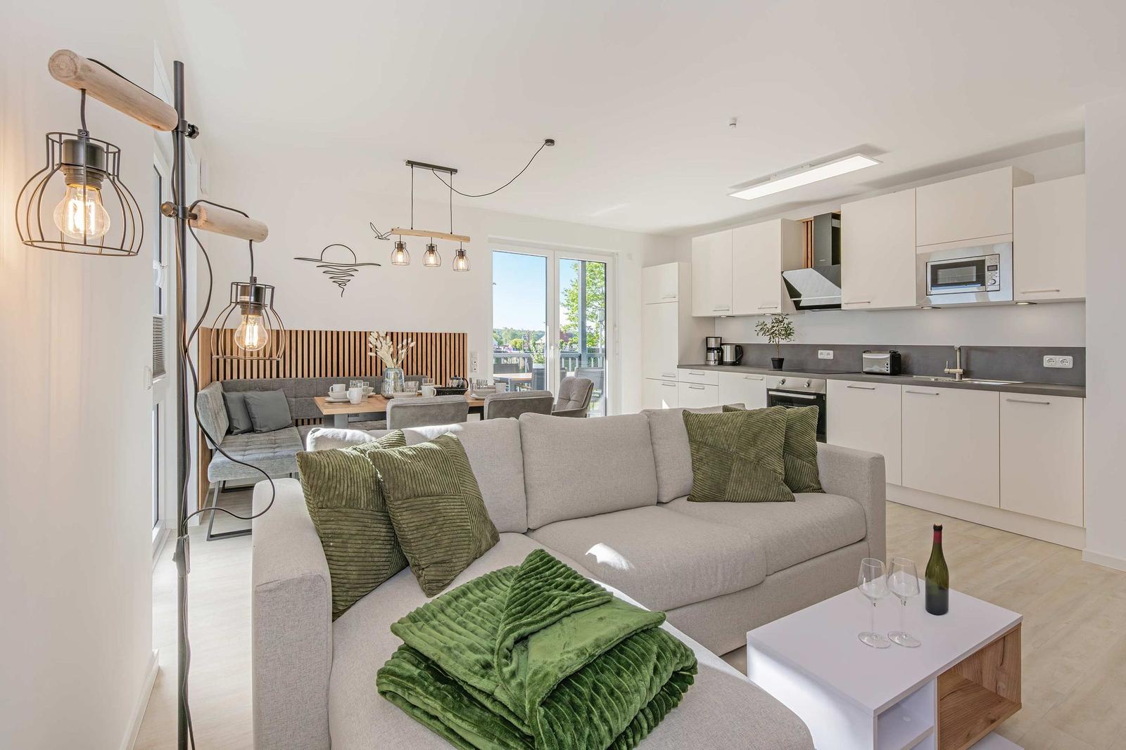 Wohnzimmer mit Sofa, Küchenzeile und Balkonansicht.