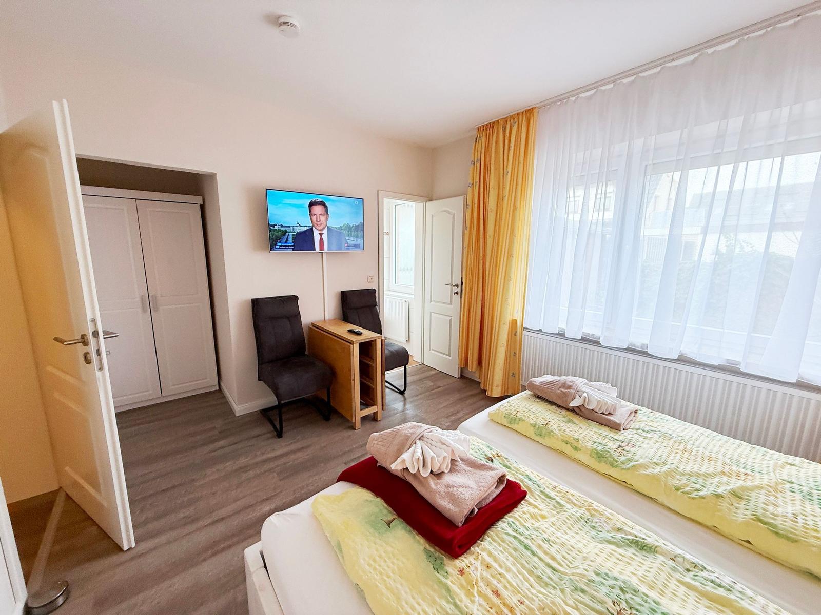 Zimmer mit zwei Betten, TV, Schrank und Fenster mit Vorhängen.