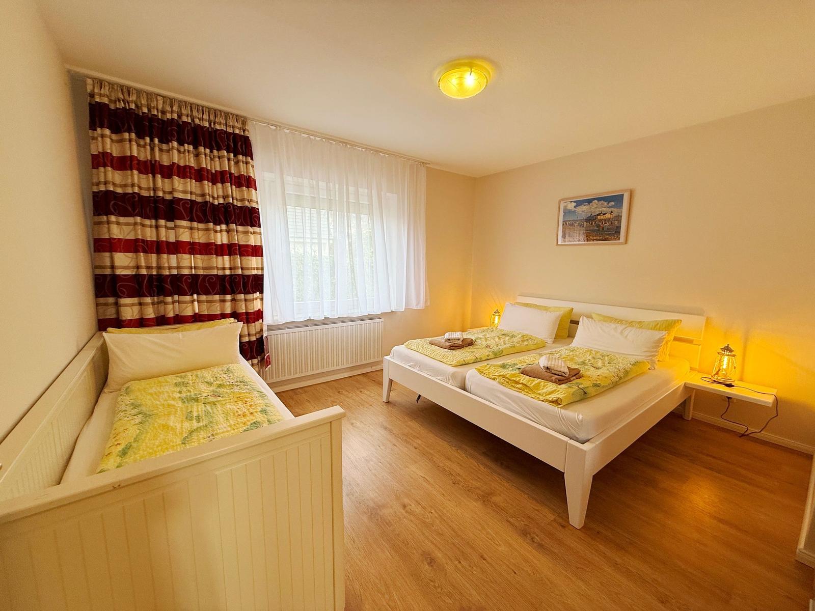 Ein Schlafzimmer mit zwei Betten, Holzboden und Fenster mit Vorhängen.