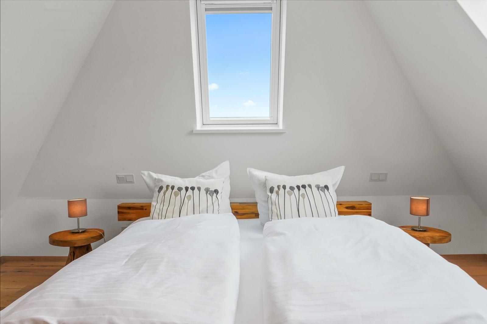 Doppelbett mit weißen Bettwäsche und Holz Nachttischen unter einem Dachfenster.
