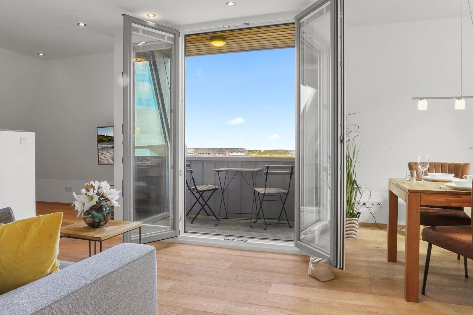 Wohnbereich mit Balkon, Tisch und Stühlen. Holzboden und große Fenster.