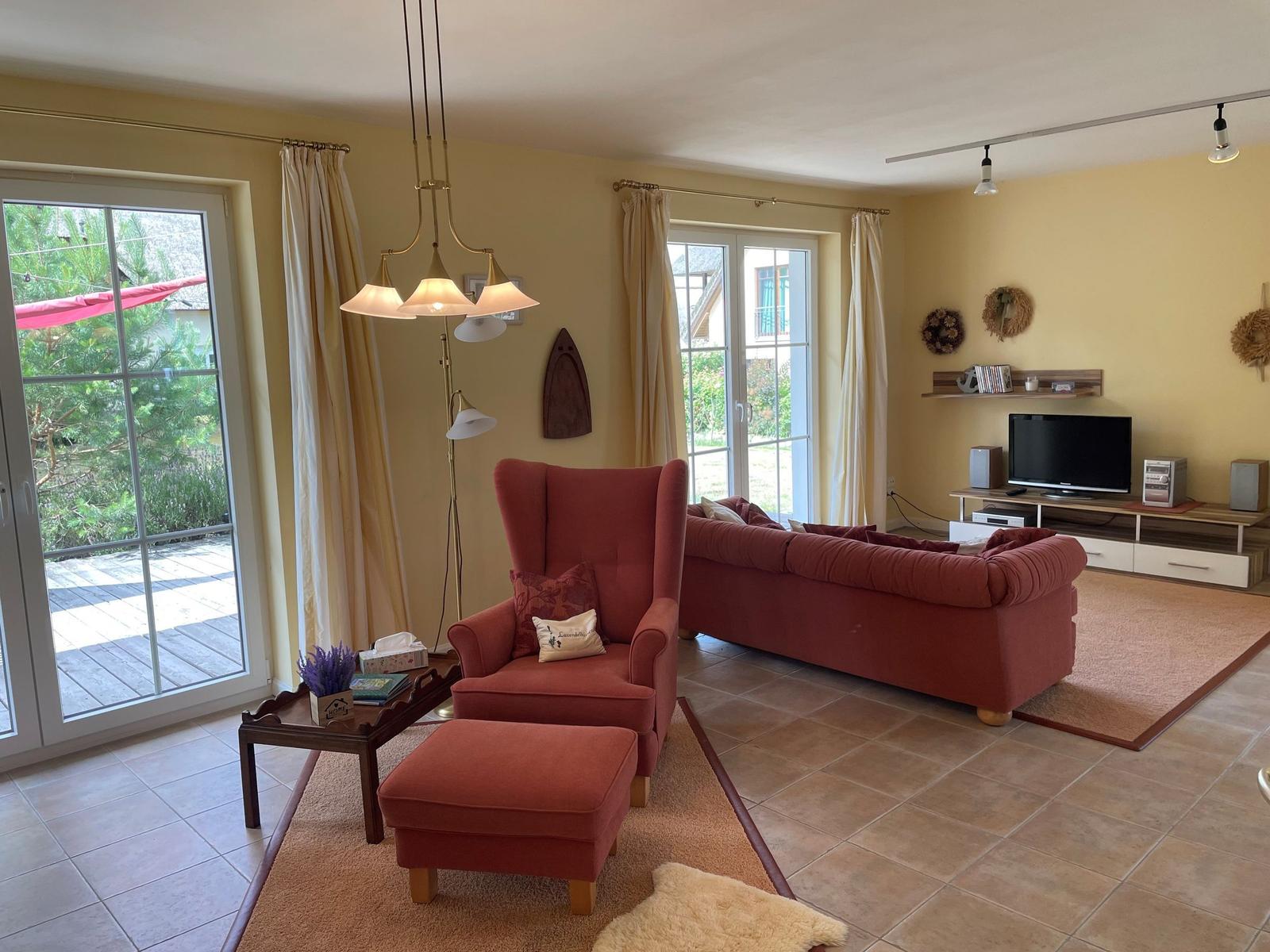 Living room with red armchair, sofa, and TV. Doorways to terrace and garden.