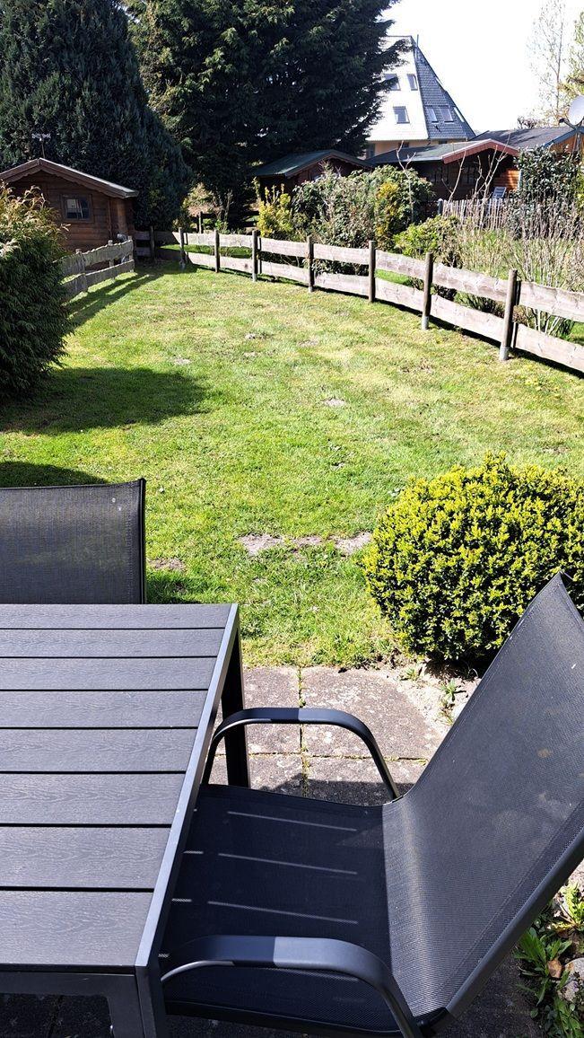 Garten mit Gartenmöbeln, Holzzaun und Grasfläche. Im Hintergrund sind Bäume und Häuser sichtbar.