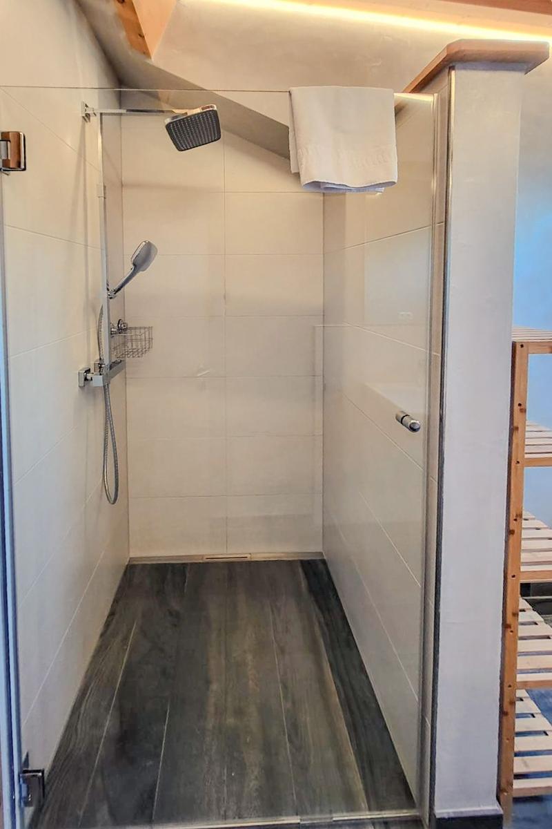 Shower cabin with overhead and handheld shower, dark floor, and white wall tiles.