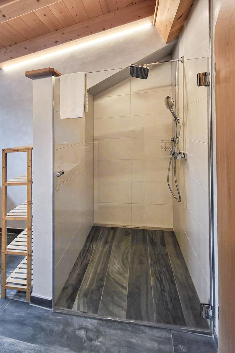 Dusche mit Glaswand, Holzboden und Duschkopf. Links steht ein hölzerner Regal.