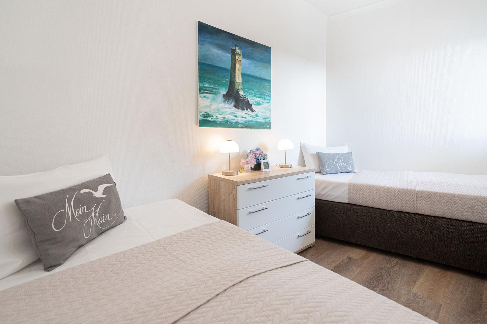 Zwei Betten mit Kissen und Nachttisch mit Lampe und Bild an der Wand.