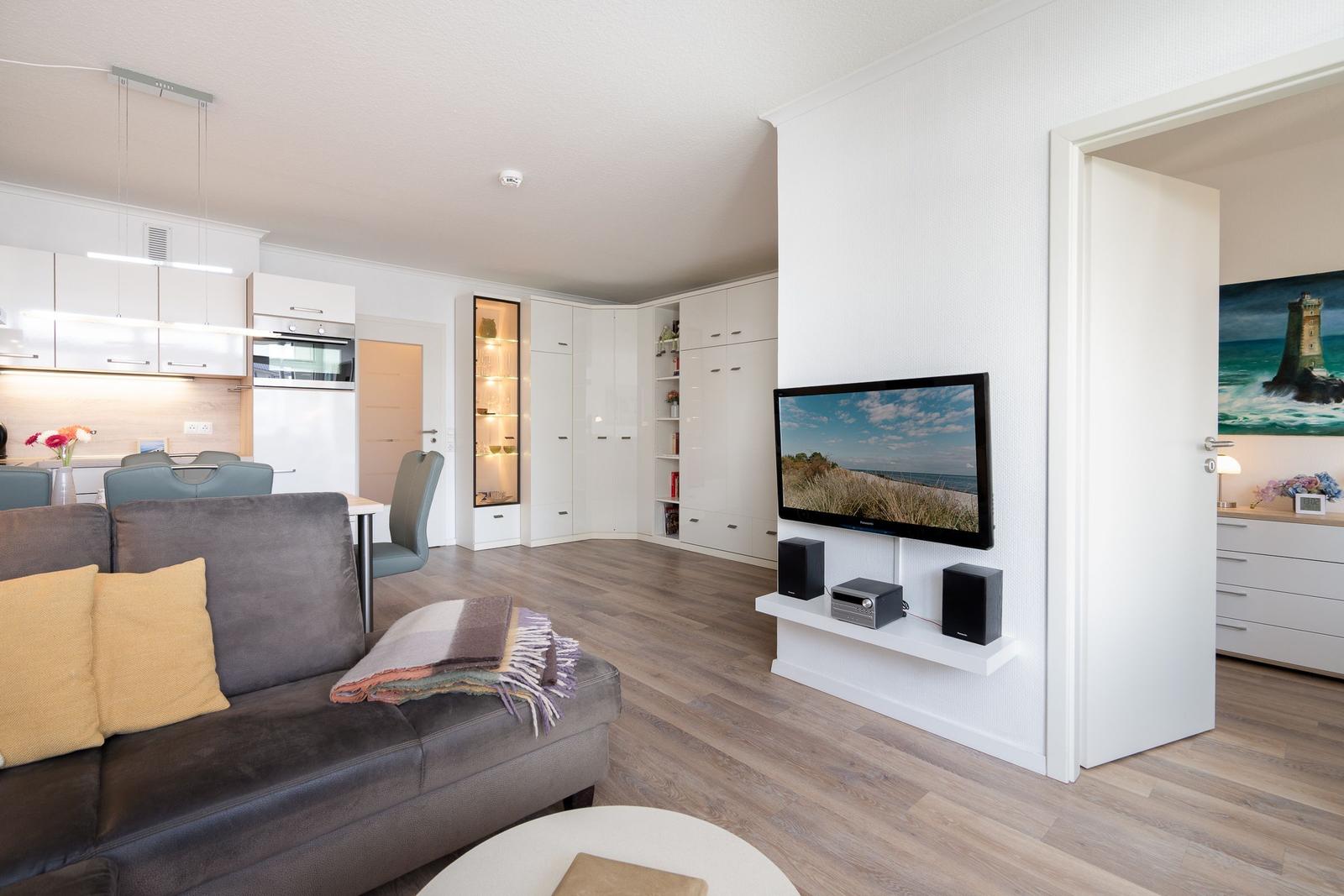 Wohnzimmer mit Sofa, Fernseher und Küchenbereich im Hintergrund.