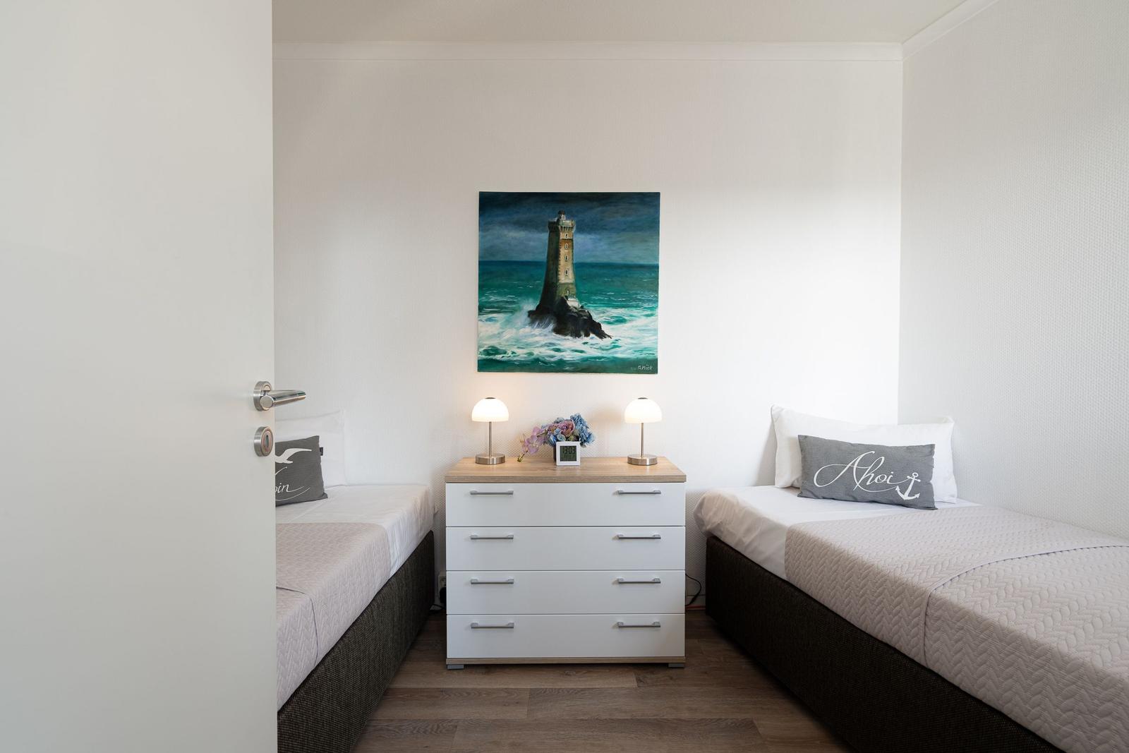 Zwei Betten flankieren einen Schrank mit Lampen und einer Leuchtturm-Bildwand.