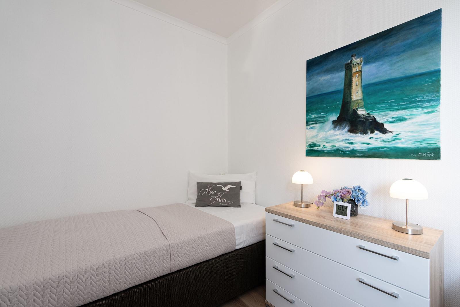 Ein Schlafzimmer mit Bett, Nachttisch und Wandbild eines Leuchtturms.